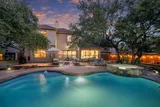 Pool and hot tub glowing at dusk behind a two-story home with warm patio lighting